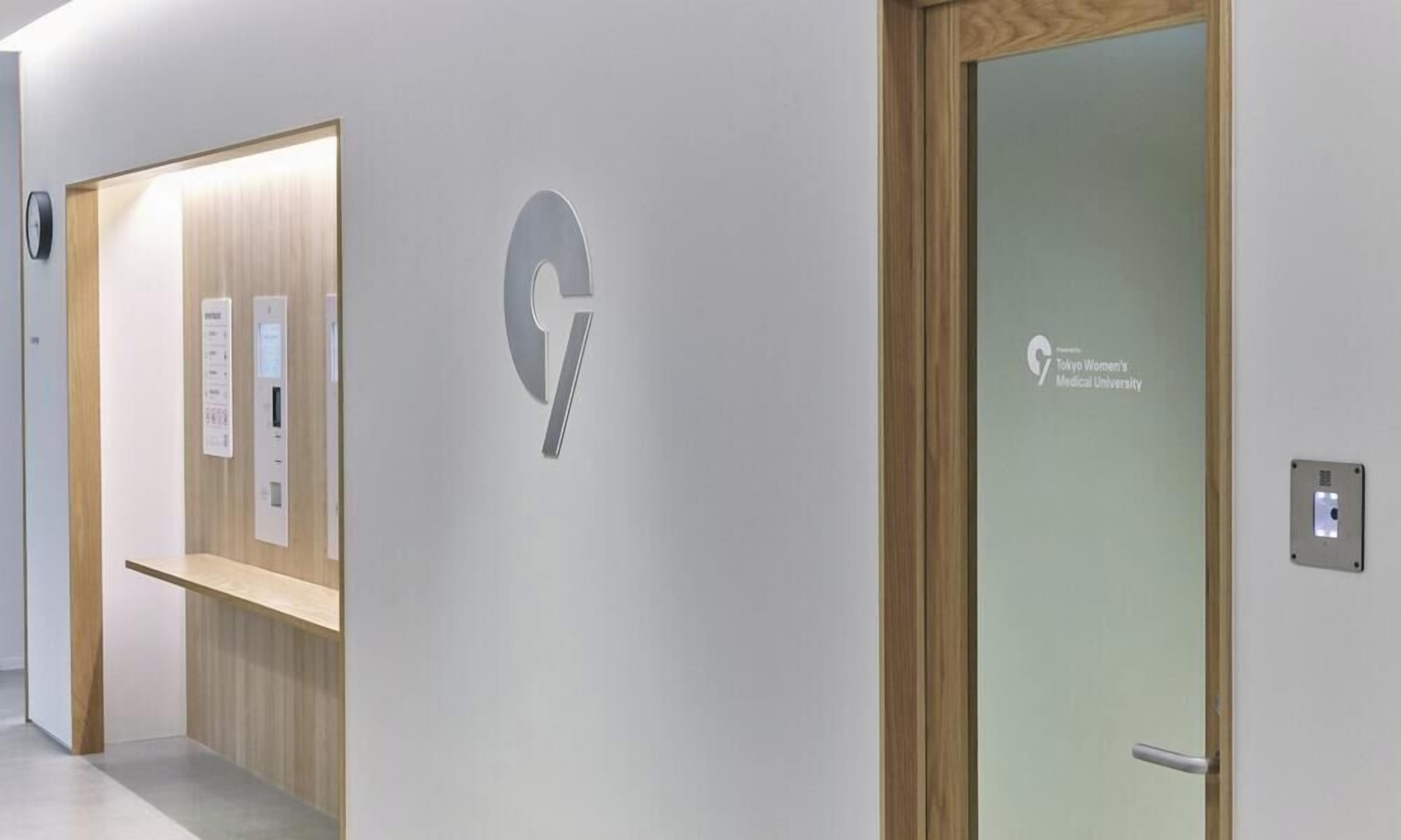 A hallway with a wooden door, a wall-mounted elevator, and a sign for Tokyo Women's Medical University.