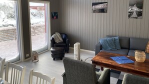 Een kamer met een eettafel, stoelen, een bank, een raam en een wandheater.