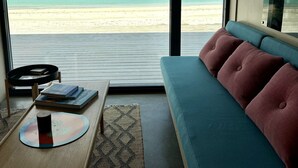 A room with a large window overlooking a beach, a sofa, a small table with books, and a tray.