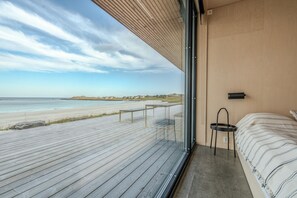 A bedroom with a large window overlooking a beach, a bed, and a small table. - Exclusive Beach House Ramberg – Your Private Oasis (Flakstad)