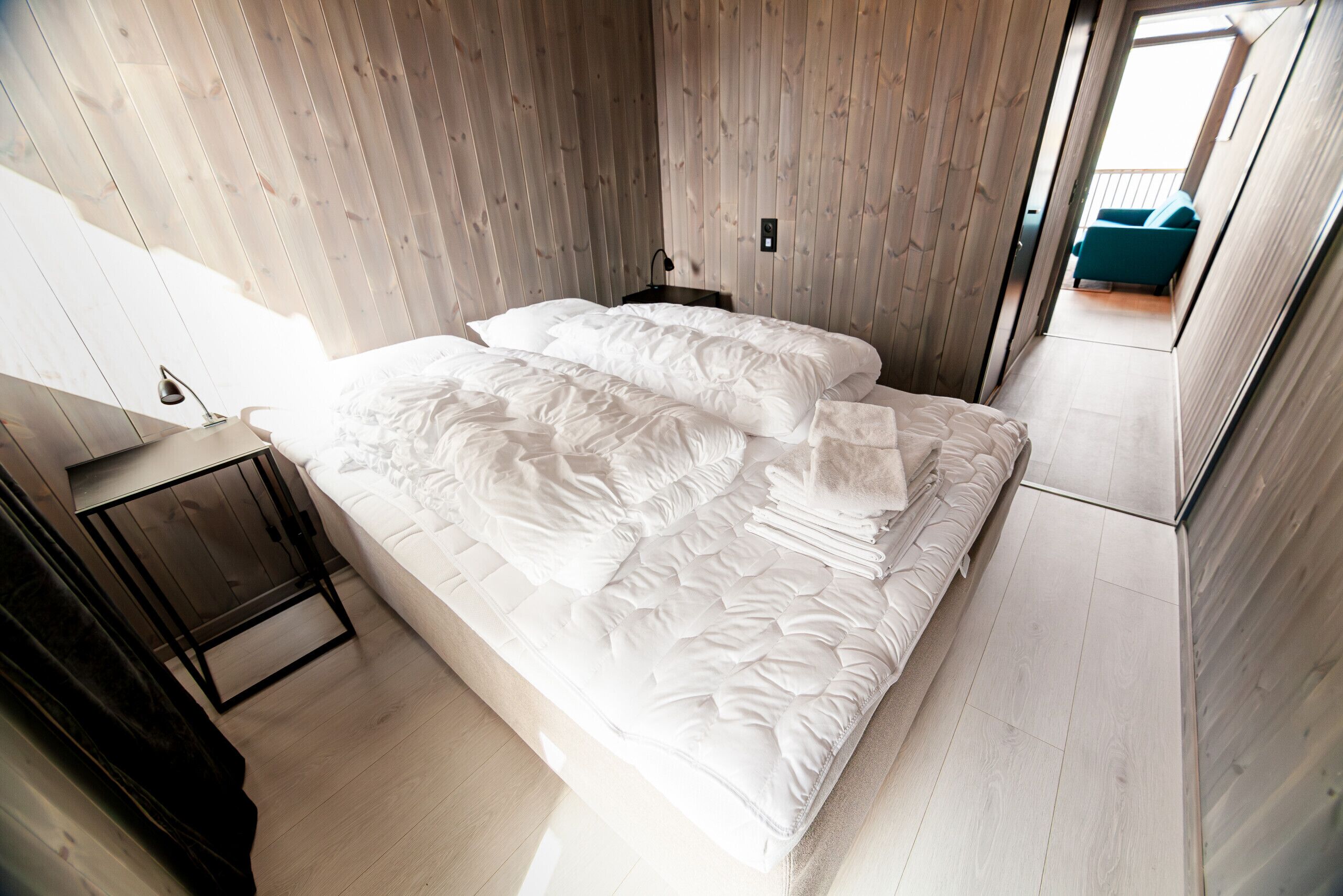 A bedroom with a large bed, a bedside table, and a view to an outdoor balcony.