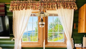 Interior rústic d'una cabana amb una taula de menjador, cadires, una espelmeta, un aparell de ràdio i una vista per la finestra.