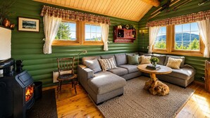 A cozy cabin interior with a fireplace, green walls, wooden ceiling, and a sofa set.
