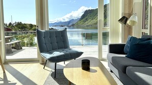 A modern living room with a view of a lake and mountains, a grey sofa, a blue armchair, and a coffee table.