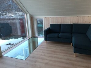 Ein modernes Wohnzimmer mit Glasboden, einem dunklen Sofa und Wandverkleidungen aus Holz.