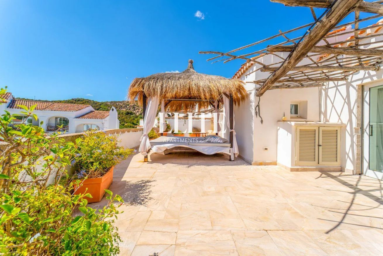 A courtyard with a thatched gazebo, potted plants, and a tiled floor.