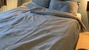 Une chambre à coucher avec un lit, des oreillers, un luminaire fixé au mur et une couronne décorative.