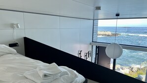 Un dormitorio moderno con una cama grande, vistas al mar y una pared blanca.