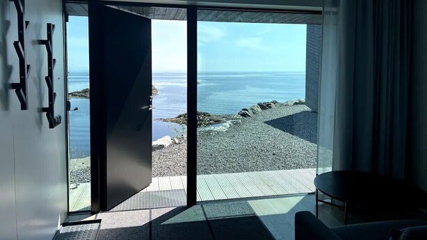 Una habitación con un amplio ventanal corredera que da a un balcón con vistas al mar y a las rocas.