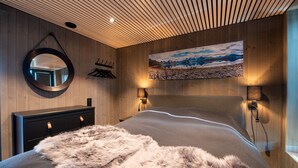 Ein Schlafzimmer mit Holzboden, einem runden Spiegel, einem Bett mit flauschiger Decke, einem Bild an der Wand und zwei Wandleuchten.