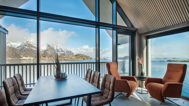 Ein moderner Essbereich mit einem großen Tisch und Ledersesseln, mit Blick auf eine malerische Berg- und Wasserlandschaft.