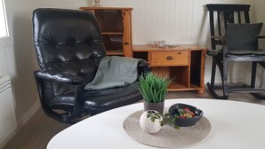A room with a white round table, a black leather chair, a wooden side table, and a black rocking chair.