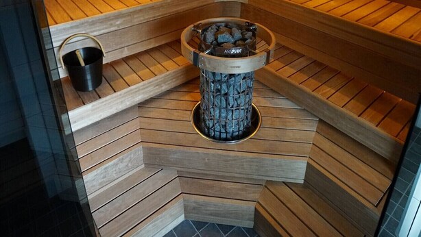 A sauna with wooden walls and a central stone feature. - Lofoten panoramic luxury home with sauna (Moskenes)