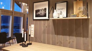 A dining area with a wooden table, two framed pictures, a shelf with jars, and a candle holder. - Magic views and walking distance to best beaches (Vestvågøy)