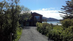 A two-story house with a balcony, a gravel driveway, and a view of a lake and mountains.