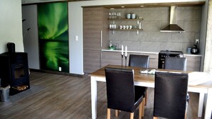 A modern kitchen with a dining area, a wood-burning stove, and a green abstract wall.