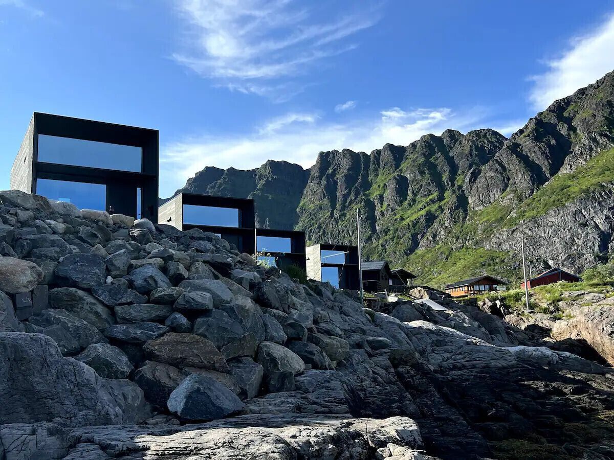 Un bâtiment moderne doté de grandes fenêtres en verre, situé sur le flanc d’une colline rocheuse, avec une chaîne de montagnes en arrière-plan.