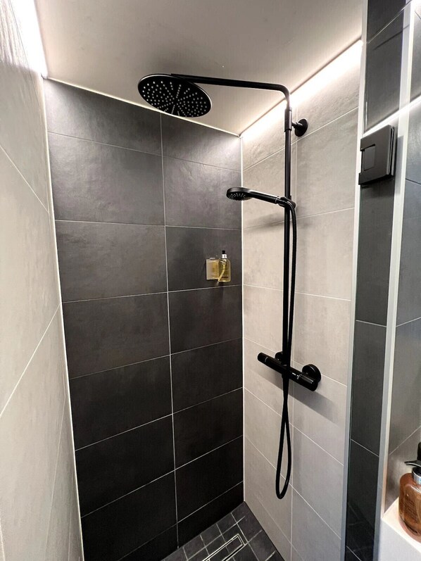 A shower with a handheld showerhead, a wall-mounted control, and a handheld hose.
