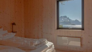 A bedroom with a bed, a nightstand, a window with a mountain view. - Minkfarmen: Spacious seaside cabin w/scenic view (Flakstad)