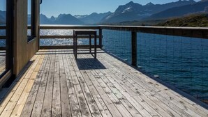 A wooden deck with a bench, overlooking a calm lake and mountains under a clear sky. - Minkfarmen: Spacious seaside cabin w/scenic view (Flakstad)