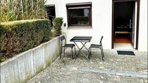Une terrasse avec une table et des chaises, une clôture en bois et l’entrée d’un bâtiment.