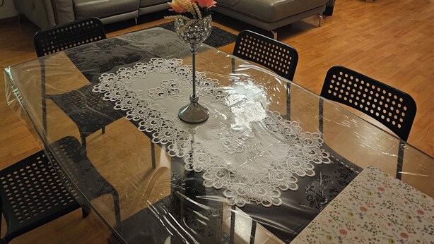 Un salon moderne avec une table à manger en verre, un canapé d’angle gris, un petit lit et un lustre décoratif.
