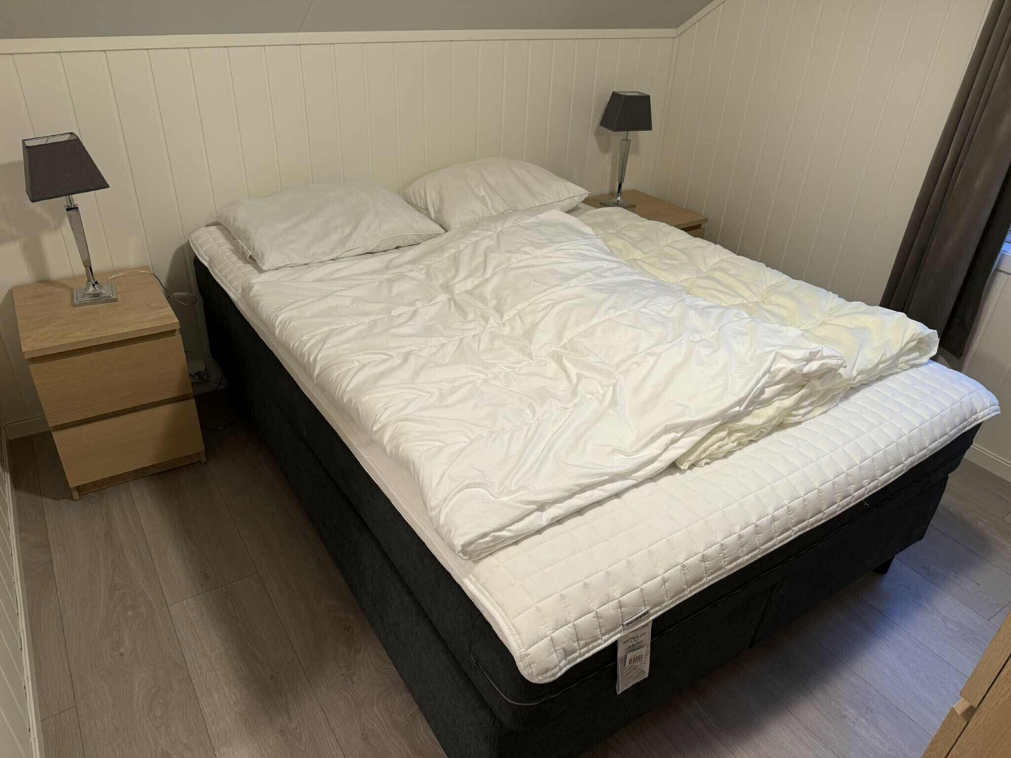 A single bed with a white duvet, two bedside tables with lamps, and a wooden floor.