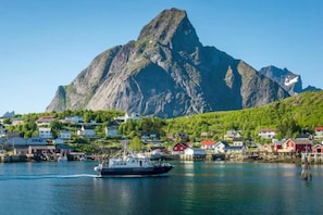 A coastal town with a prominent mountain in the background, a harbor with boats, and houses with red roofs. - Madelhea Cabin- Seaview Lodge (Moskenes)