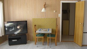 Une pièce avec un téléviseur posé sur un meuble, une petite table avec des chaises, une lampe et une porte donnant sur une autre pièce.