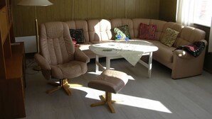 Un salon comprenant un canapé, un fauteuil, un pouf et une table basse.
