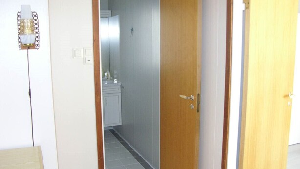 Une pièce avec une porte en bois, un mur blanc et un sol carrelé.