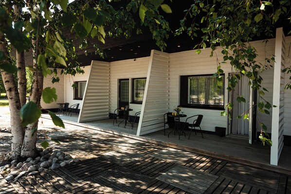 A covered outdoor area with wooden flooring, tables, chairs, and a stone pathway.