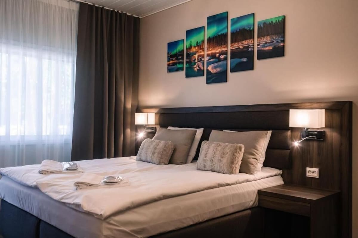 A hotel room with a large bed, two bedside lamps, a headboard, and a wall with four framed pictures.
