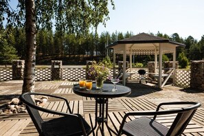 A wooden deck with a gazebo, outdoor seating, and a table with drinks.