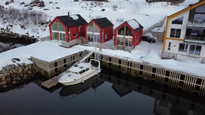 Une propriété située au bord de l’eau, comprenant trois cabanes rouges, un quai et un bâtiment blanc doté de grandes fenêtres.