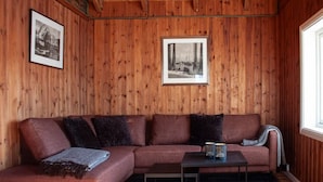 A wooden-paneled room with a sectional sofa, a small table, and two framed pictures on the wall.