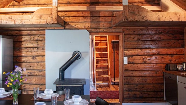 A rustic cabin interior with a dining area, a wood-burning stove, and a kitchen.