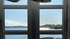 Una ventana con vista a una costa rocosa y agua tranquila.