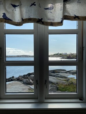 A window with a view of a rocky shoreline and calm water. - Nordlandshus ved havet på Reine, Lofoten (Moskenes)