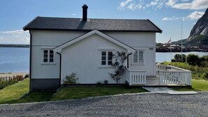 Una casa blanca de dos pisos con techo negro, un porche pequeño y vista al mar.