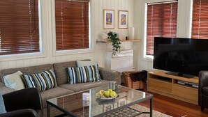 Una sala de estar con un sofá, una mesa de centro de vidrio, un televisor y suelo de madera.