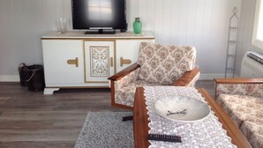Ein Wohnzimmer mit Fernseher auf einem Schrank, gemustertem Sessel und Couchtisch mit Gläsern und Fernbedienung.