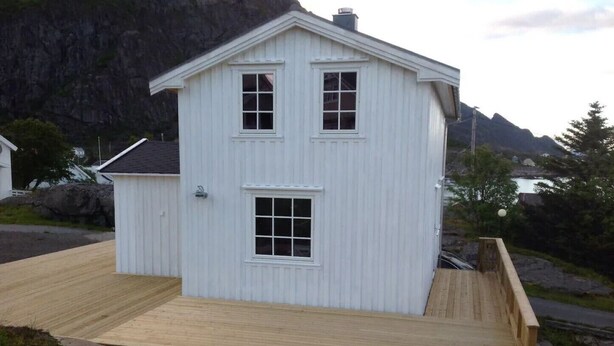 Ein weißes Holzhaus mit Satteldach, einer Veranda und einer kleinen Terrasse.