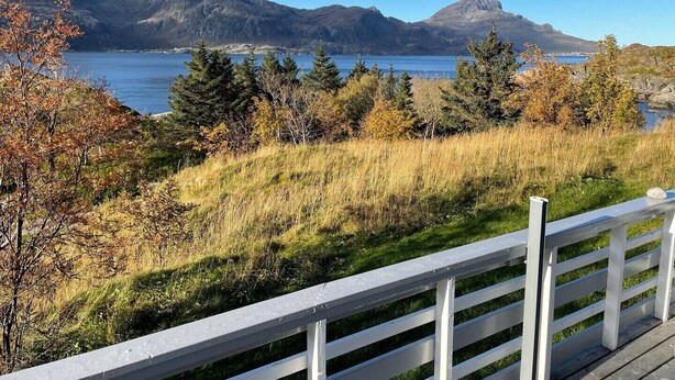 A coastal landscape with mountains, a body of water, and a white fence.