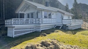 A white cabin with a deck, surrounded by trees and mountains.