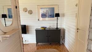 A room with a wooden floor, a round rug, a gray cabinet with a bowl and glasses, a framed picture on the wall, and a door with a mirror.