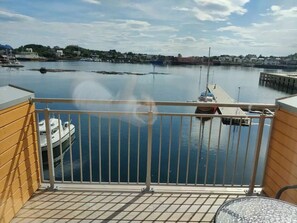 Ein Balkon mit Blick auf einen ruhigen Hafen, ein Boot an der Mole und ein Steg in der Ferne.