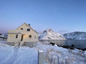 A two-story house with a balcony, a staircase, and a view of a mountain and lake. - House in Reine by the Fjord (Moskenes)