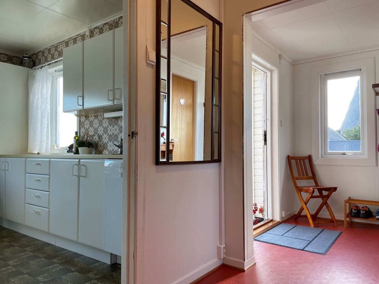A kitchen with white cabinets, a mirror, a wooden chair, and a small table with shoes.