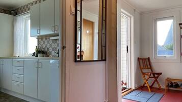 A kitchen with white cabinets, a mirror, a wooden chair, and a small table with shoes.
